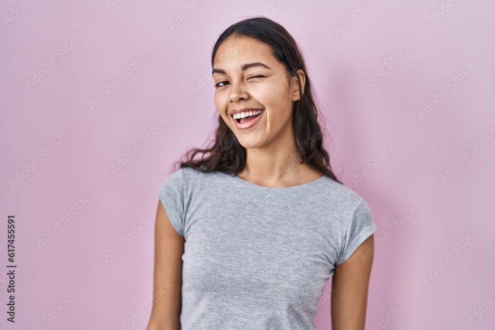 Young brazilian woman wearing casual t shirt over pink background winking looking at the camera with sexy expression, cheerful and happy face. Young brazilian woman wearing casual t shirt over pink background winking looking at the camera with sexy expression, cheerful and happy face.