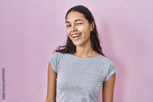 Young brazilian woman wearing casual t shirt over pink background winking looking at the camera with sexy expression, cheerful and happy face.