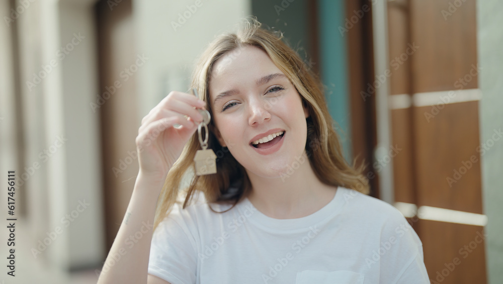 Young caucasian woman smiling confident holding key of new home at street