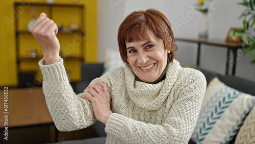 Mature hispanic woman smiling confident doing strong gesture with arm at home