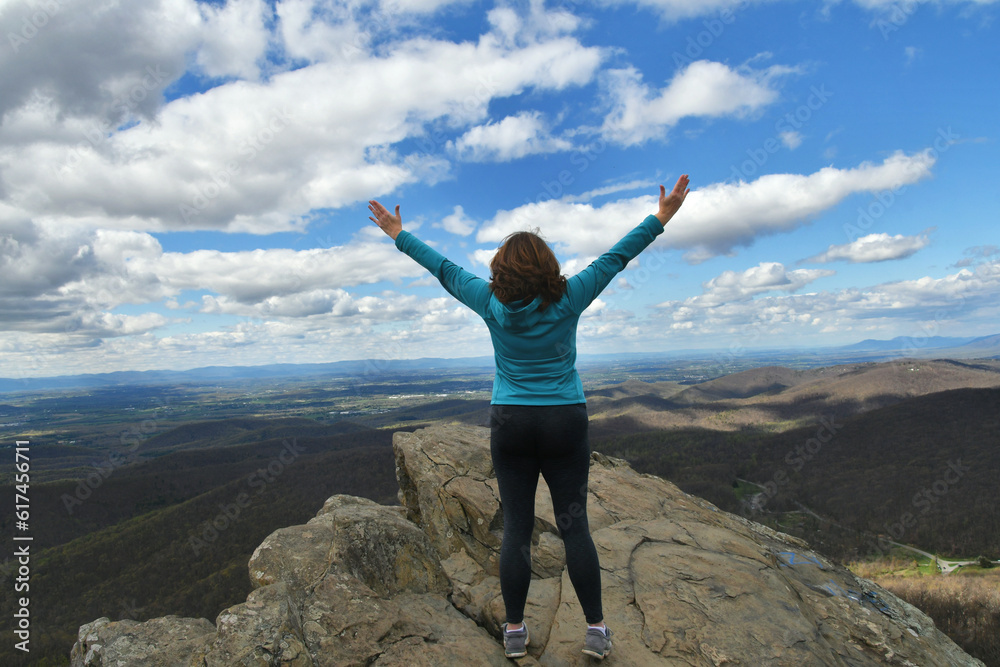Middle-age woman standing on rock ledge arms in air celebrating success, victory Middle-age woman standing on rock ledge arms in air celebrating success, victory