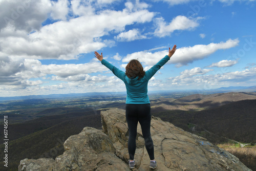 Middle-age woman standing on rock ledge arms in air celebrating success, victory
