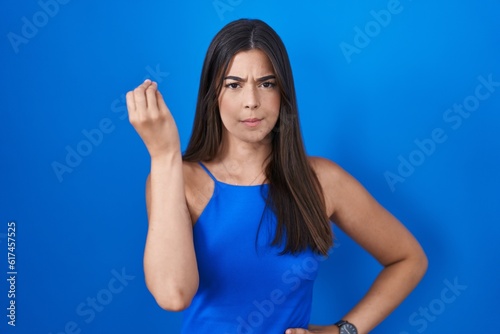 Hispanic woman standing over blue background doing italian gesture with hand and fingers confident expression