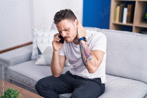 Young hispanic man talking on smartphone with worried expression at home