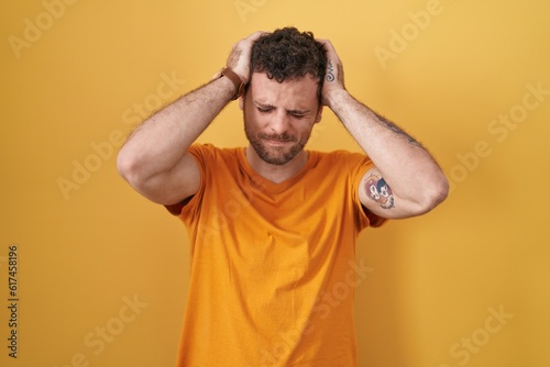 Young hispanic man standing over yellow background suffering from headache desperate and stressed because pain and migraine. hands on head. © Krakenimages.com