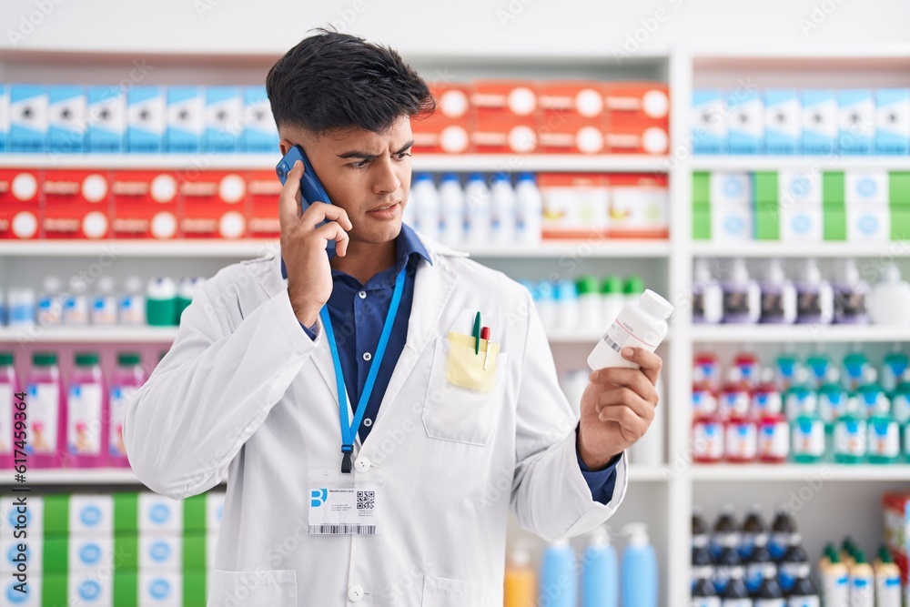 Young hispanic man pharmacist holding pills bottle talking on smartphone at pharmacy Young hispanic man pharmacist holding pills bottle talking on smartphone at pharmacy