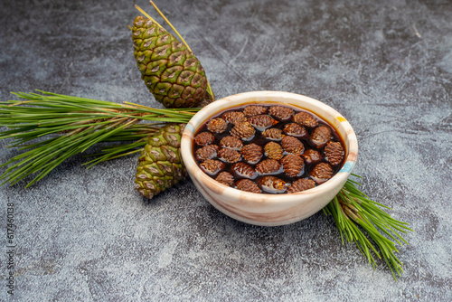 Fototapeta Naklejka Na Ścianę i Meble -  Young pine cones jam in glass bowl on gray marble background. Delicious jam with small pine cones.