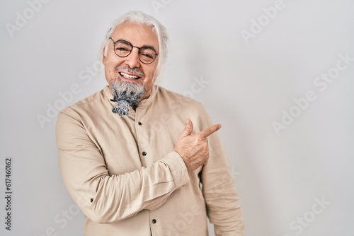 Middle age man with grey hair standing over isolated background cheerful with a smile of face pointing with hand and finger up to the side with happy and natural expression on face