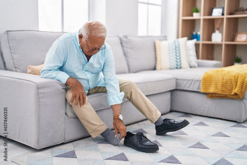 Senior grey-haired man suffering for feet pain sitting on sofa at home Senior grey-haired man suffering for feet pain sitting on sofa at home
