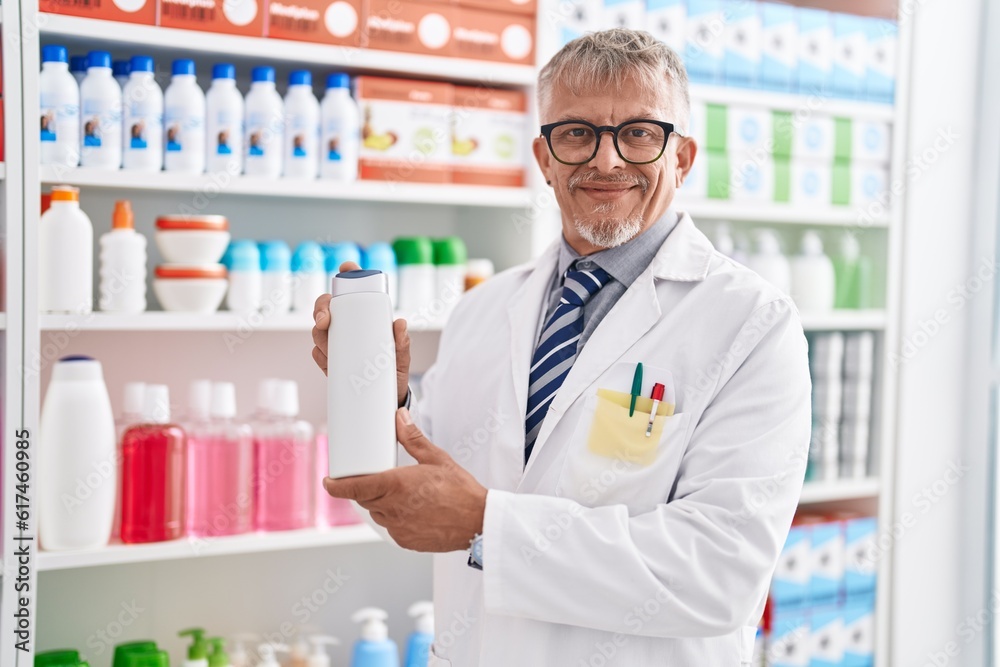 Middle age grey-haired man pharmacist holding shampoo bottle at laboratory