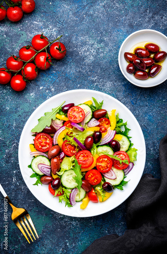 Tasty salad with kalamata olives, tomatoes, paprika, cucumber and onion, healthy mediterranean food. Blue table background, top view