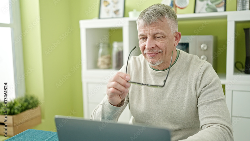 Middle age grey-haired man using laptop sitting on table at home Middle age grey-haired man using laptop sitting on table at home