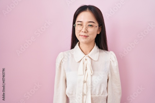 Young chinese woman standing over pink background winking looking at the camera with sexy expression, cheerful and happy face.