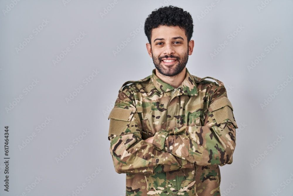 Arab man wearing camouflage army uniform happy face smiling with crossed arms looking at the camera. positive person.