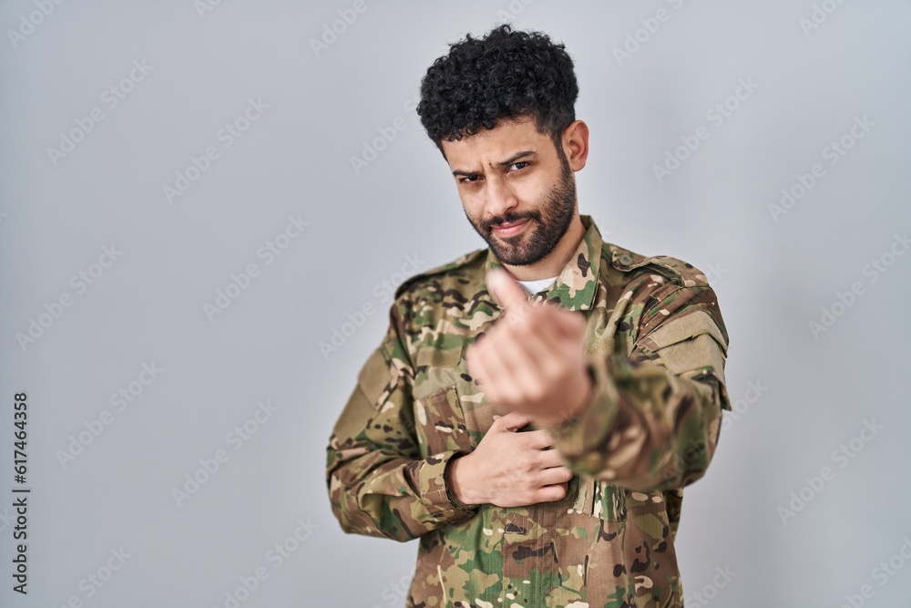 Arab man wearing camouflage army uniform beckoning come here gesture with hand inviting welcoming happy and smiling