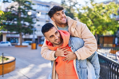 Two man couple hugging each other holding boyfriend on back at park