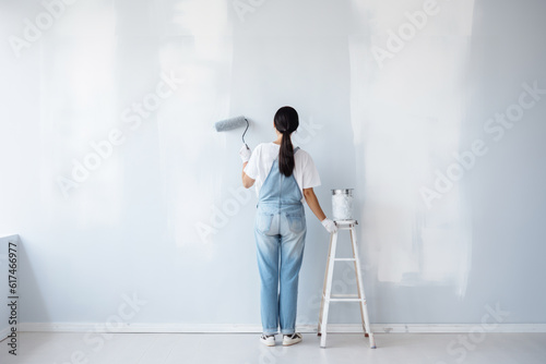 A woman in denim overalls paints a wall with a roller. Photorealistic illustration of Generative AI.