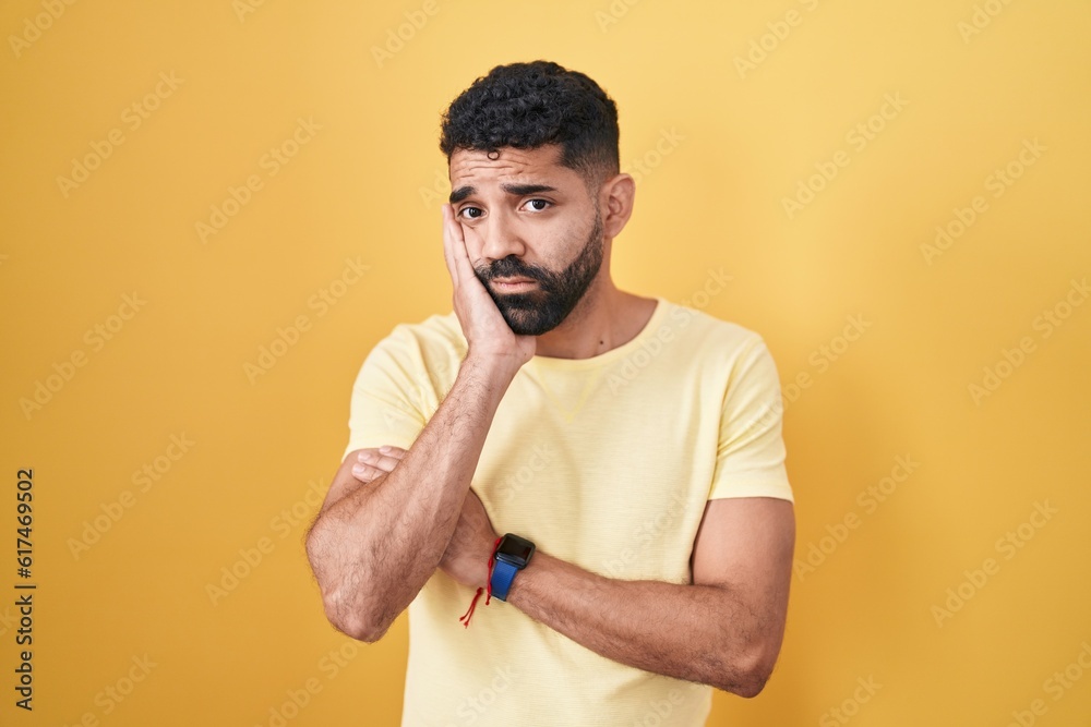 Hispanic man with beard standing over yellow background thinking looking tired and bored with depression problems with crossed arms. Hispanic man with beard standing over yellow background thinking looking tired and bored with depression problems with crossed arms.