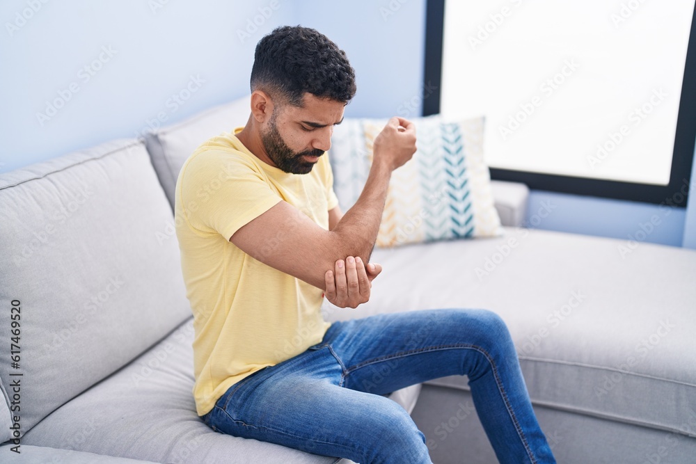 Young arab man sitting on sofa suffering for elbow pain at home