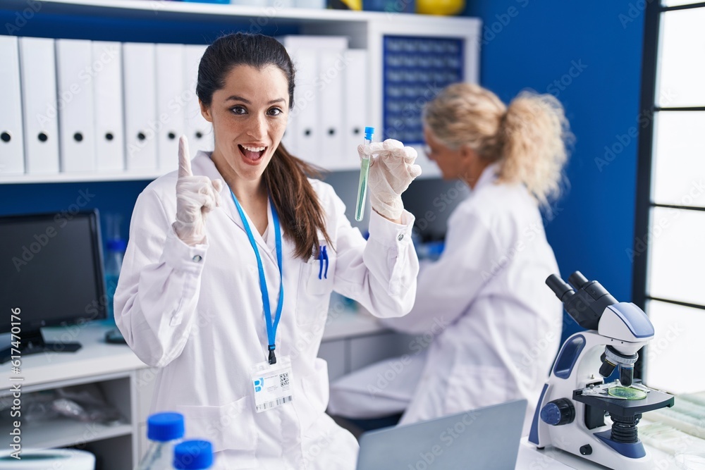 Young hispanic woman working at scientist laboratory surprised with an idea or question pointing finger with happy face, number one