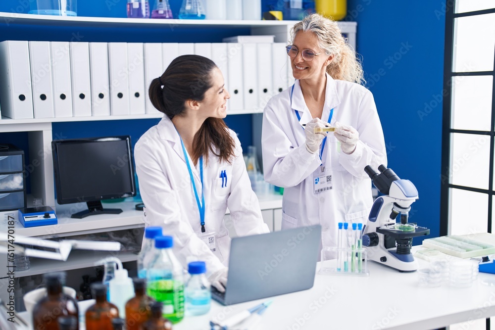 Two women scientists using laptop writing on urine test tube at laboratory Two women scientists using laptop writing on urine test tube at laboratory