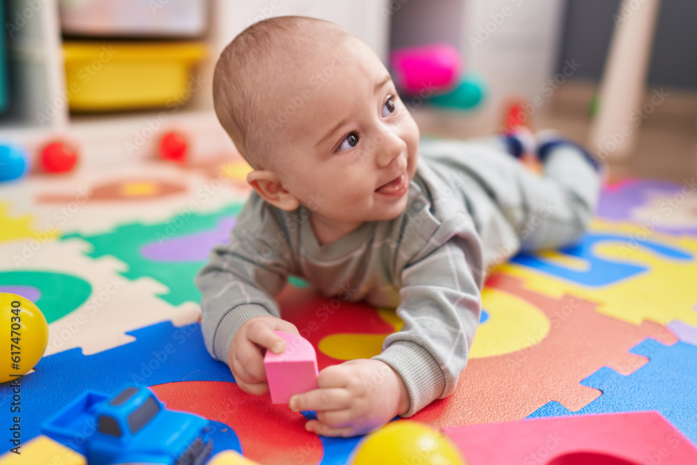 Obraz premium Adorable caucasian baby smiling confident lying on floor at kindergarten