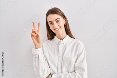 Young caucasian woman standing over isolated background smiling looking to the camera showing fingers doing victory sign. number two.