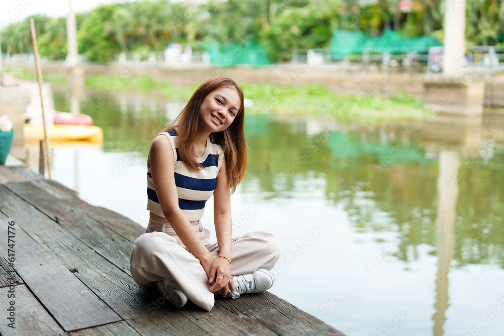 Cute Asian girl with long hair sitting and relaxing in her free time on the pier By the river on weekends with smiling faces A rural canal with clear water