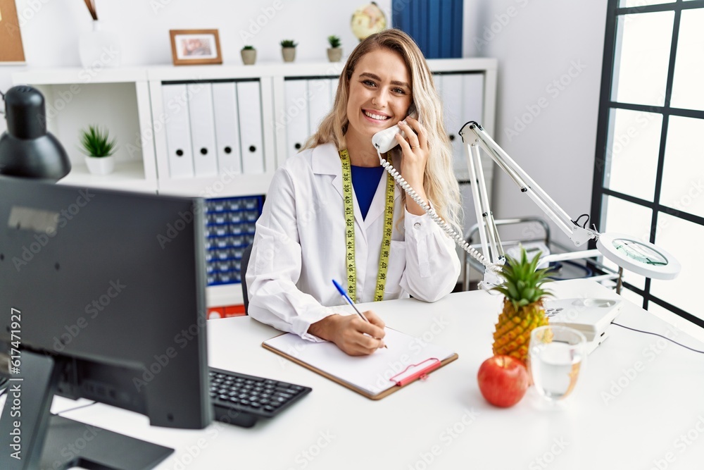 Young woman dietician talking on telephone writing on document at clinic Young woman dietician talking on telephone writing on document at clinic