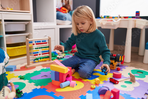 Adorable caucasian boy playing with car toy and construction blocks sitting on floor at kindergarten