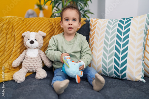 Adorable hispanic boy sitting on sofa playing with elephant toy at home