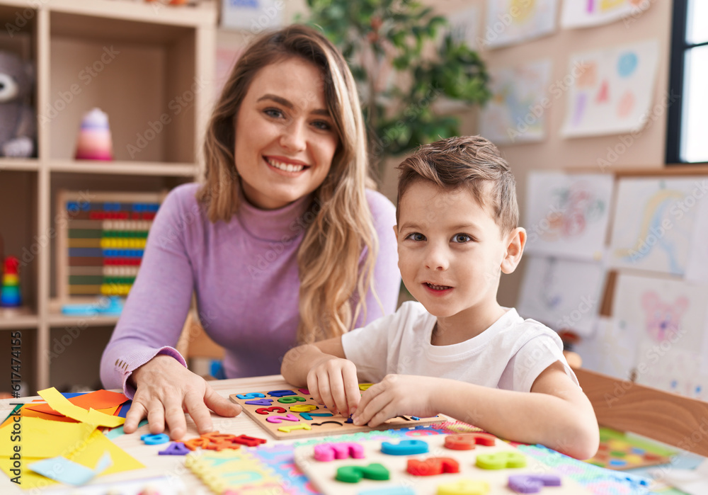 Fototapeta premium Woman and boy playing with maths puzzle game sitting on table at kindergarten
