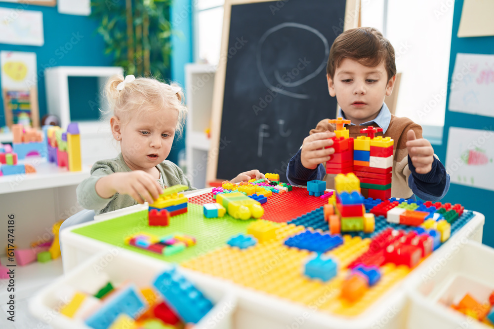 Fototapeta premium Adorable boy and girl playing with construction blocks sitting on table at kindergarten