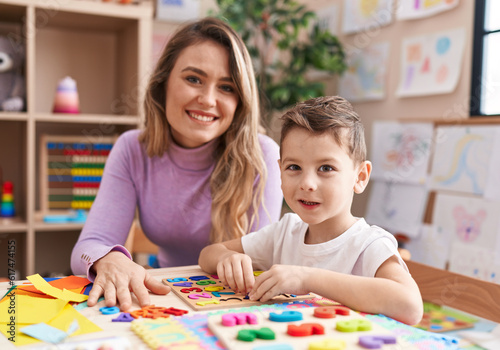 Woman and boy playing with maths puzzle game sitting on table at kindergarten