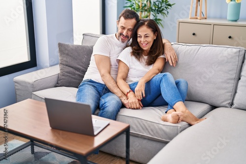 Middle age man and woman couple watching movie sitting on sofa at home