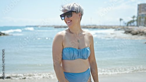 Fototapeta Naklejka Na Ścianę i Meble -  Young woman tourist wearing bikini and sunglasses smiling at beach