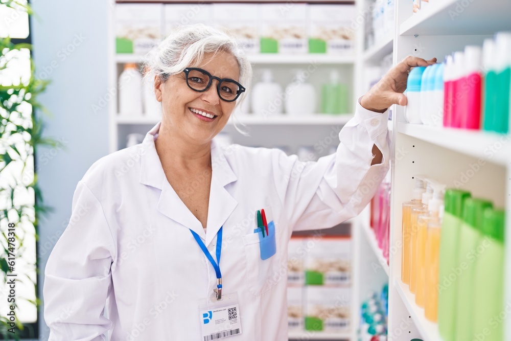 Middle age grey-haired woman pharmacist holding deodorant bottle at pharmacy