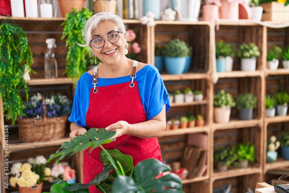 Middle age grey-haired woman florist smiling confident touching plant at florist