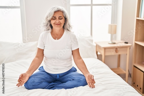 Middle age woman doing yoga exercise sitting on bed at bedroom