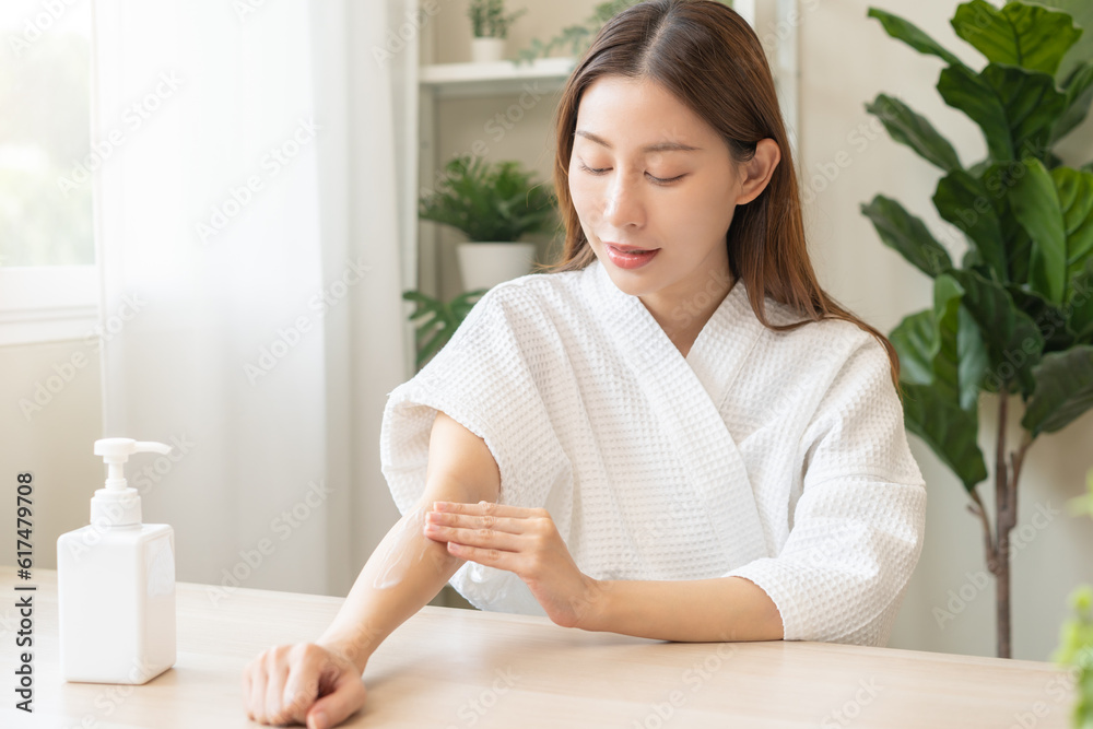 Health care, beauty smile pretty asian young woman in bathrobe, towel after shower bath at home, hand applying, putting moisturizer on her arm. Skin body cream moisturizing lotion, routine in morning. Health care, beauty smile pretty asian young woman in bathrobe, towel after shower bath at home, hand applying, putting moisturizer on her arm. Skin body cream moisturizing lotion, routine in morning.