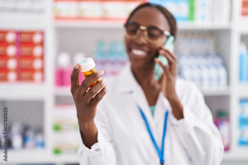 African american woman pharmacist holding pills bottle talking on smartphone at pharmacy