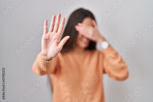 Young brunette woman standing over white background covering eyes with hands and doing stop gesture with sad and fear expression. embarrassed and negative concept.