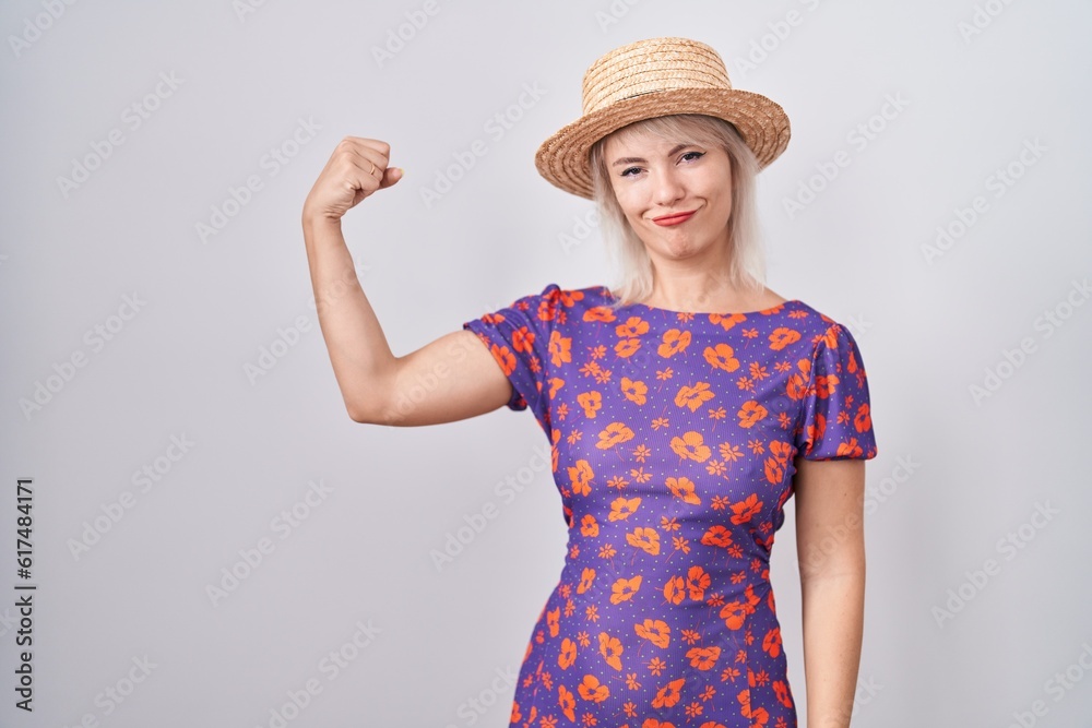 Young caucasian woman wearing flowers dress and summer hat strong person showing arm muscle, confident and proud of power Young caucasian woman wearing flowers dress and summer hat strong person showing arm muscle, confident and proud of power