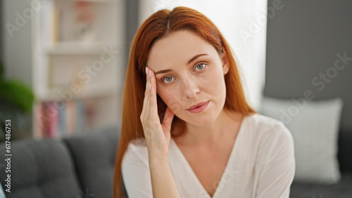 Young redhead woman sitting on sofa with serious face at home
