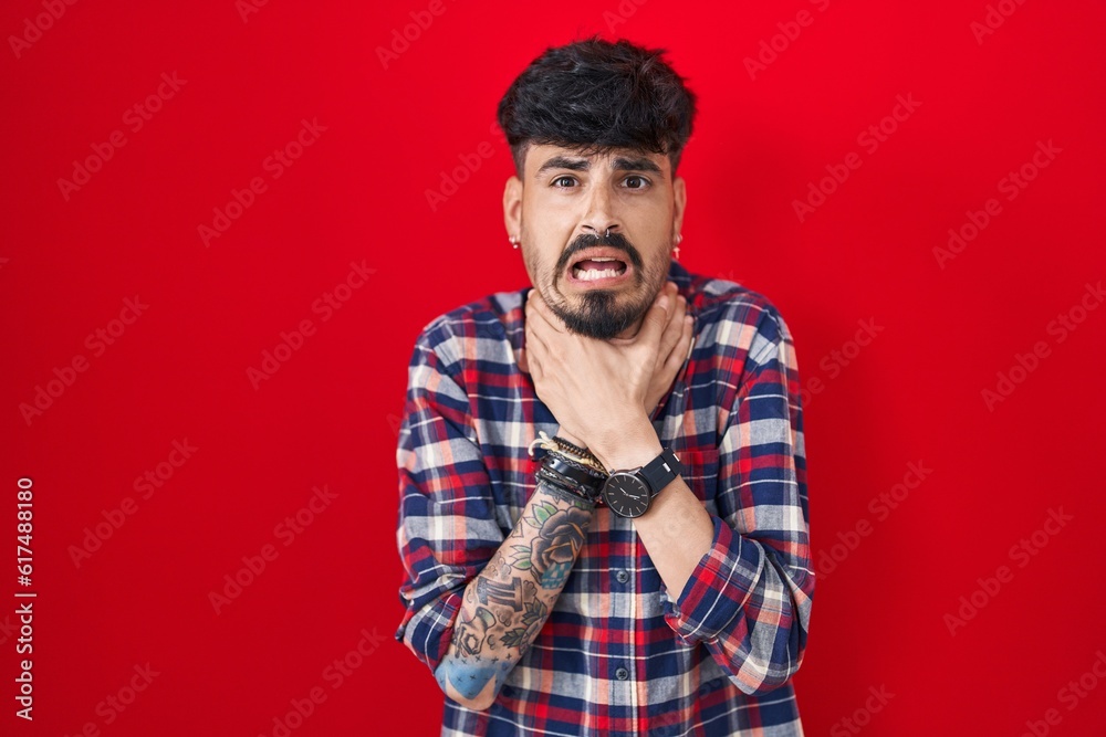 Young hispanic man with beard standing over red background shouting suffocate because painful strangle. health problem. asphyxiate and suicide concept.