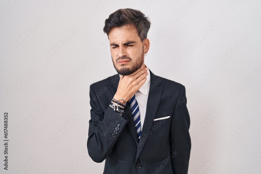 Young hispanic man with tattoos wearing business suit and tie touching painful neck, sore throat for flu, clod and infection Young hispanic man with tattoos wearing business suit and tie touching painful neck, sore throat for flu, clod and infection