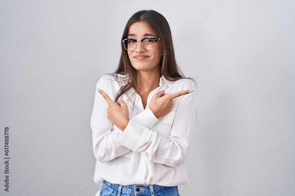 Young brunette woman wearing glasses pointing to both sides with fingers, different direction disagree Young brunette woman wearing glasses pointing to both sides with fingers, different direction disagree