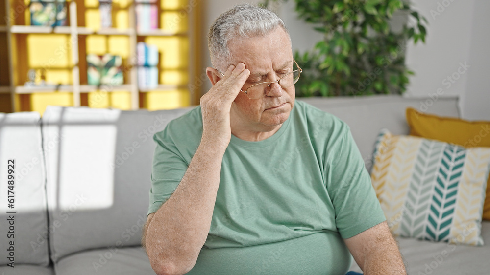 Middle age grey-haired man suffering for headache sitting on sofa at home Middle age grey-haired man suffering for headache sitting on sofa at home