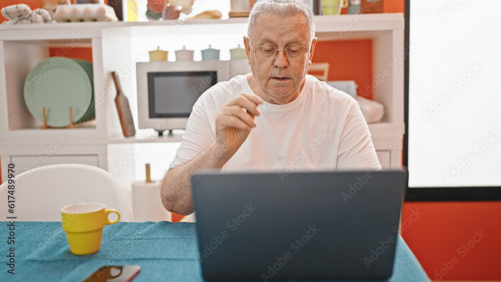 Middle age grey-haired man having video call sitting on table at dinning room Middle age grey-haired man having video call sitting on table at dinning room
