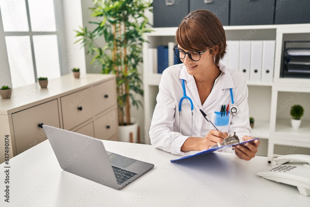 Young beautiful hispanic woman doctor using laptop writing medical report at clinic Young beautiful hispanic woman doctor using laptop writing medical report at clinic